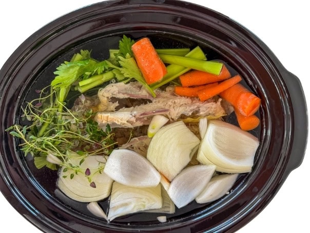 The chicken carcass, vegetables, herbs and water in the crock pot before being cooked.