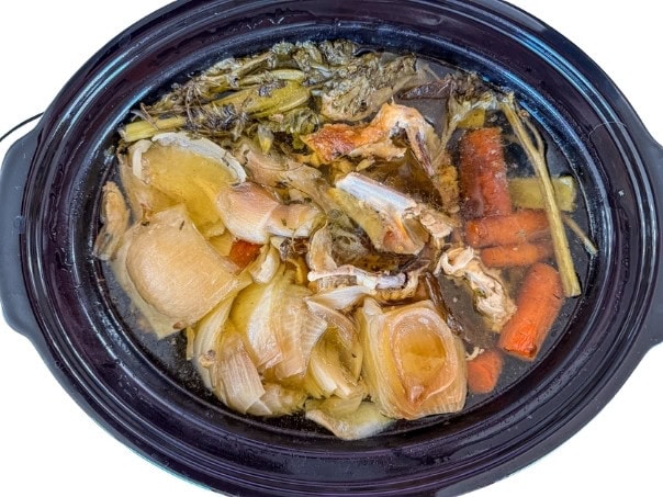 The chicken parts, vegetables, and herbs in the slow cooker after being cooked on lo for about 14 hours.