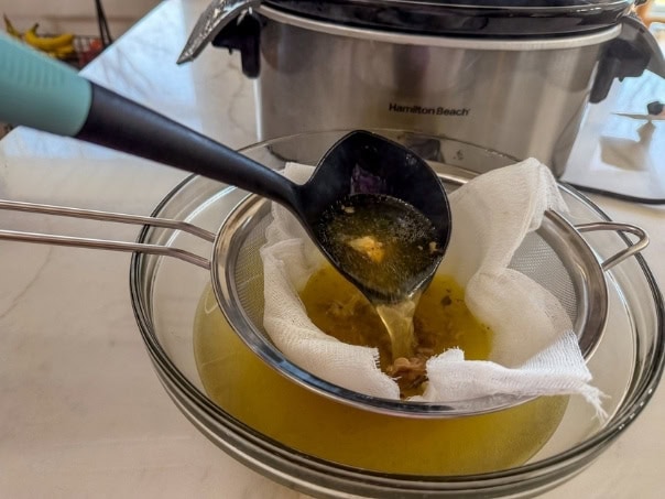 Some of the homemade chicken stock being ladled through a fie mesh stainer lined with cheesecloth.