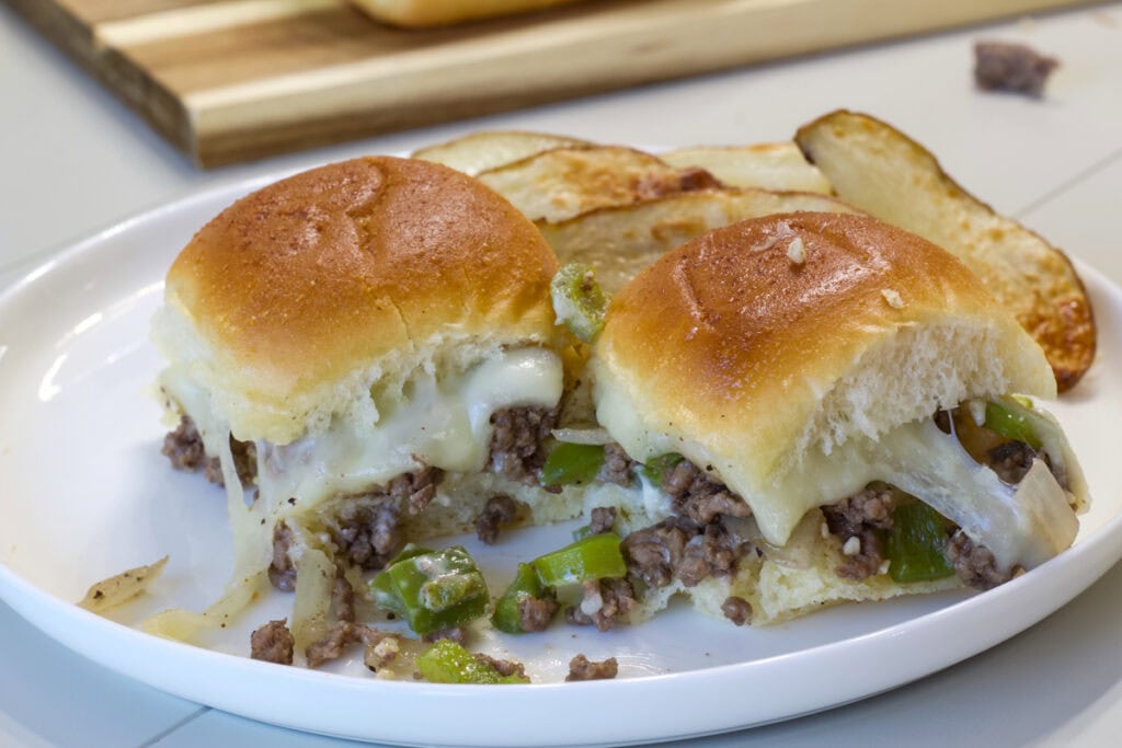 Two Ground Beef Philly Cheesesteak Sliders on a plate with some potato wedges.