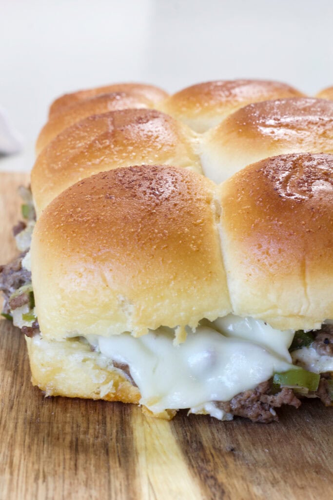 The whole batch of uncut Ground Beef Philly Cheesesteak Sliders on a wooden cutting board.
