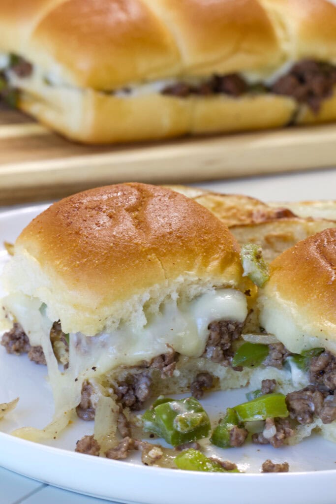 Close up of one Ground Beef Philly Cheesesteak Sliders on a plate with another slider and some of the filling on the plate in front of the slider.