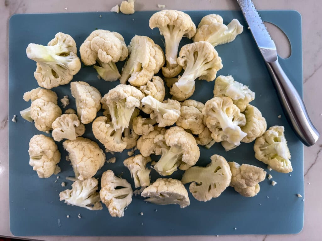 The cut up cauliflower on a cutting board.