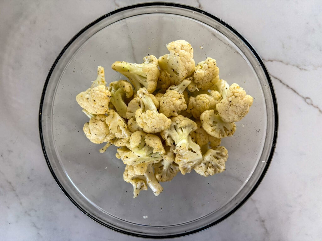 The cut cauliflower in a bowl tossed with olive oil and seasonings.