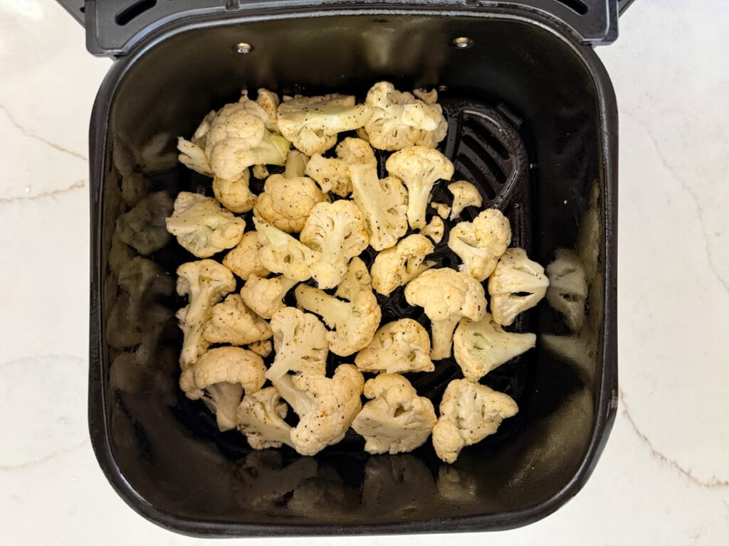 The seasoned cauliflower in the air fryer basket ready to be air fried.