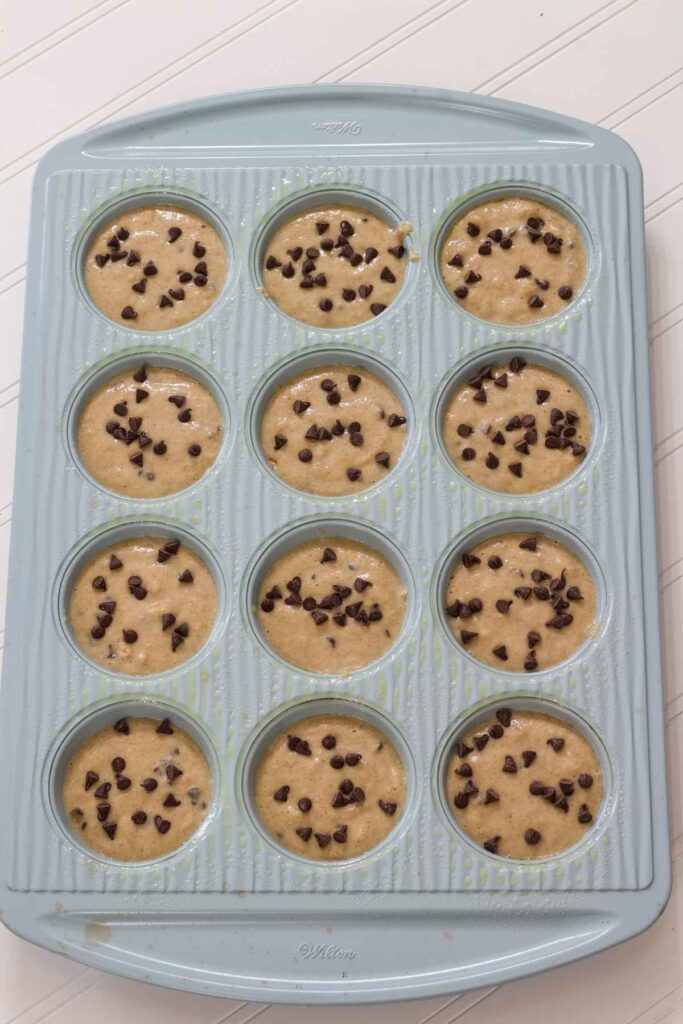 The muffin batter in the muffin tin with chocolate chips added to the top nd ready to go into the oven.