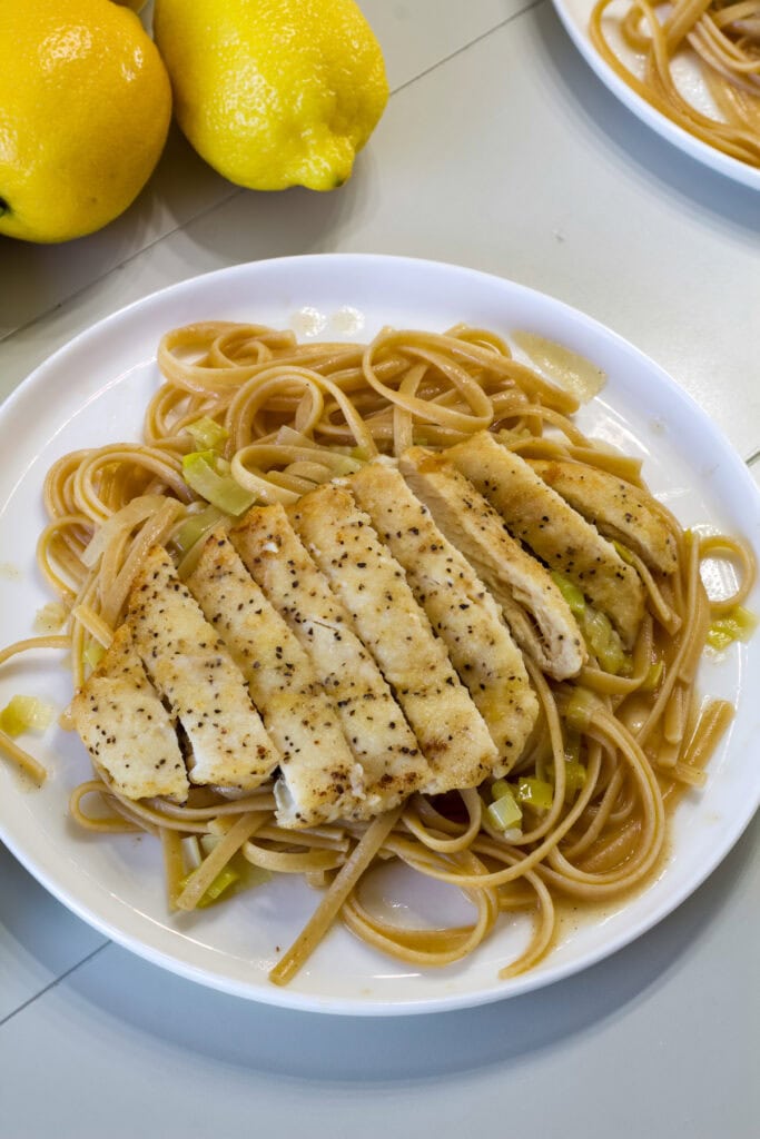 Overhead shot of one serving of Lemon Linguine with Chicken on a white plate with a couple of lemons next to it.