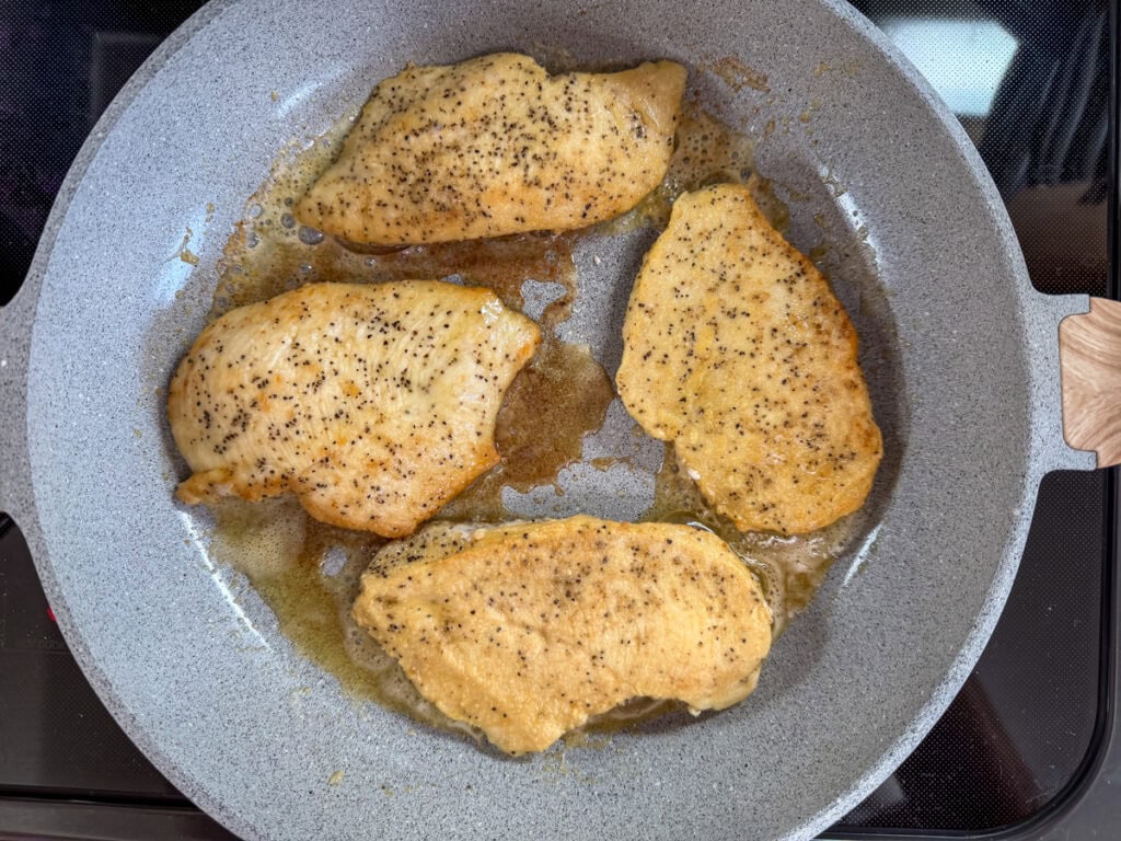 Four thinly sliced boneless skinless chicken breasts in a pan, seared side up.