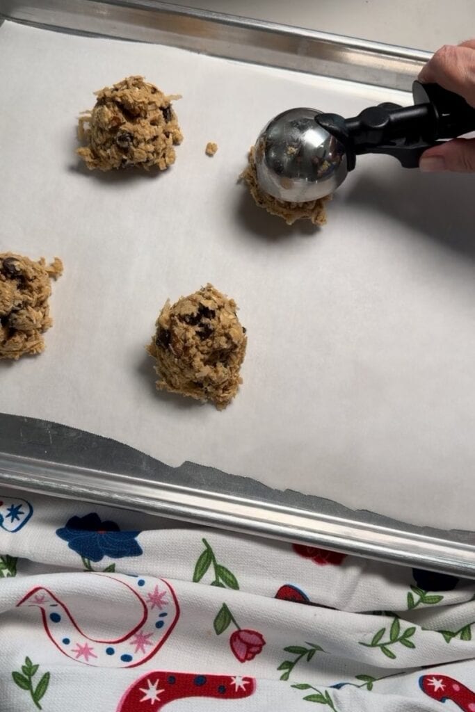 Quarter cup scoops of raw cookie dough on a parchment paper lined rimmed baking sheet.