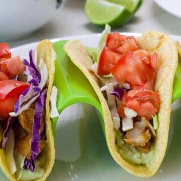 Close up of two swai fish tacos so the avocado cream, fish and toppings are visiblle.