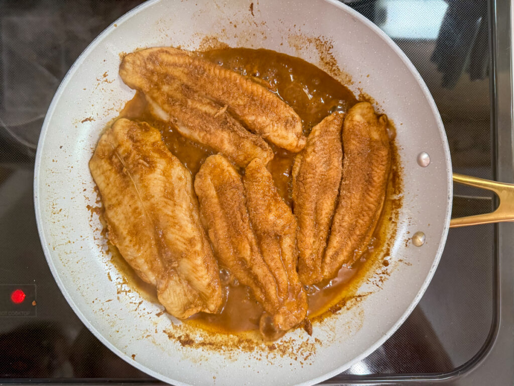 Four marinated swai fish fillets cooking in a frying pan.