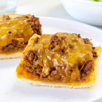 Close up side view of two pieces of Sloppy Joe Garlic Bread on a white plate.
