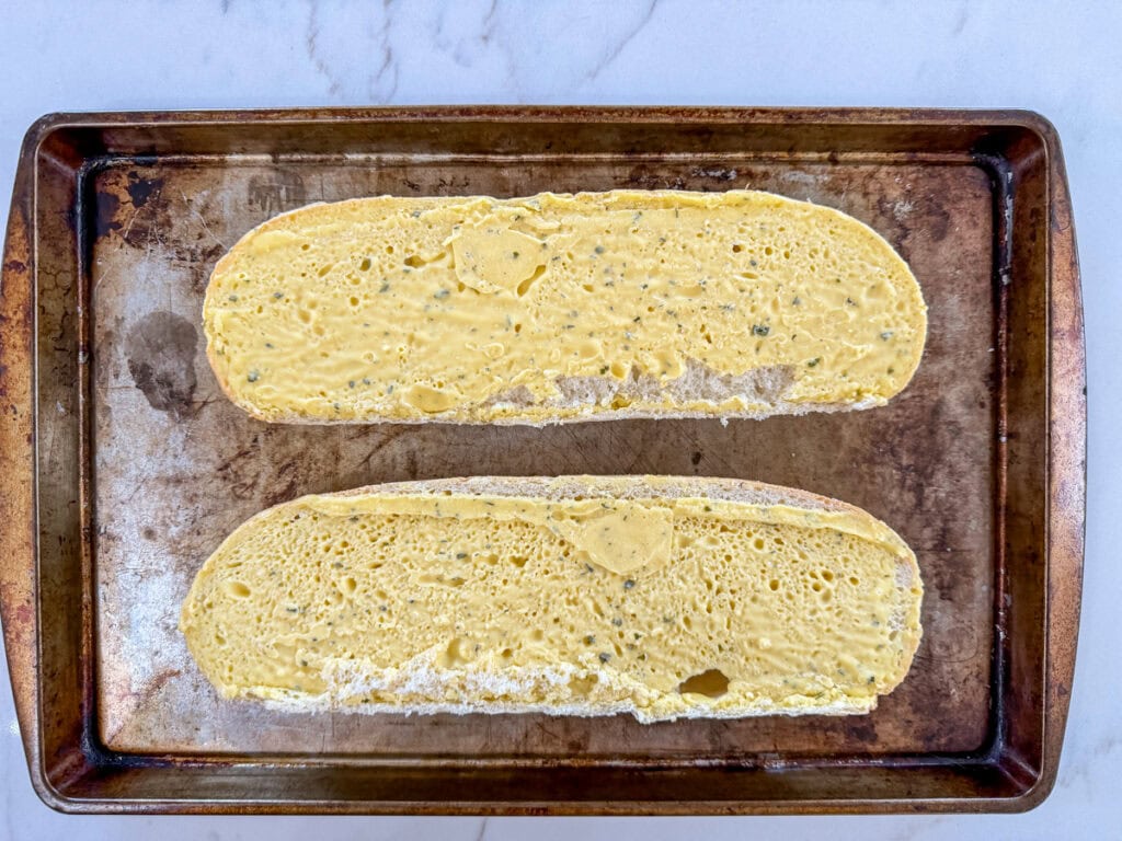 The frozen garlic bread halves on a rimmed baking sheet ready to go into the oven.