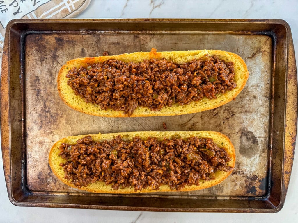 The meat mixture added to the baked garlic bread loaf halves.