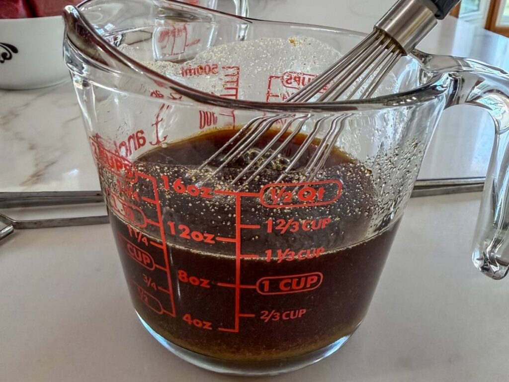 The ingredients for the sauce in a measuring cup with a whisk in it.