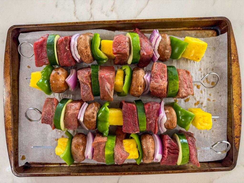 The assembled Teriyaki Beef Skewers on a parchment lined rimmed baking sheet ready to go into the oven.