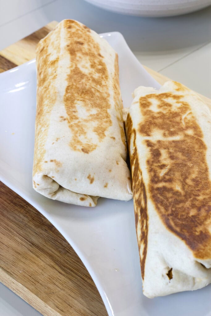Two uncut Cheesy Beef and Potato Burritos on a white plate.