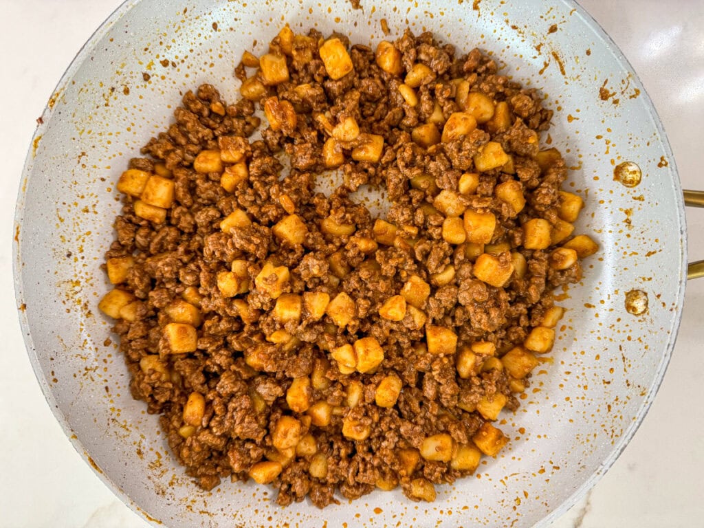 Seasoned ground beef and potato chunks after being cooked in a skillet.