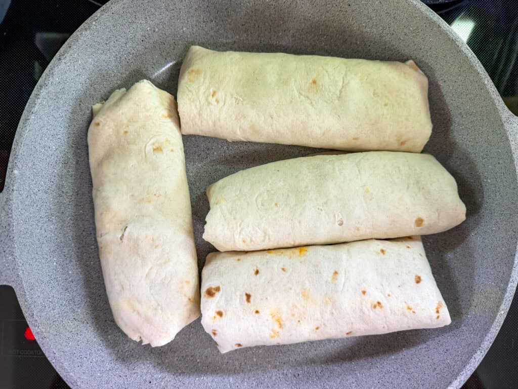 Four large Cheesy Beef and Potato Burritos in a skillet to get browned.