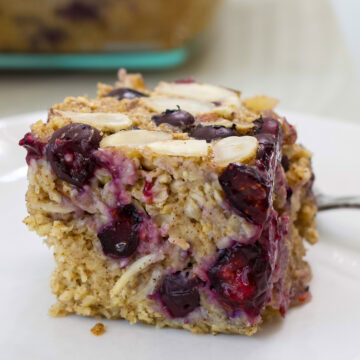 Slice of blueberry baked oatmeal topped with sliced almonds and baked blueberries on a white plate.