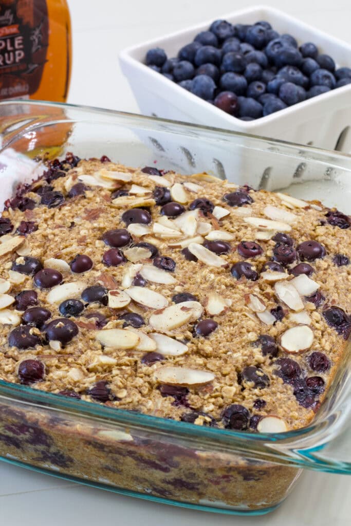 Blueberry baked oatmeal in a glass baking dish topped with fresh blueberries and sliced almonds before baking.