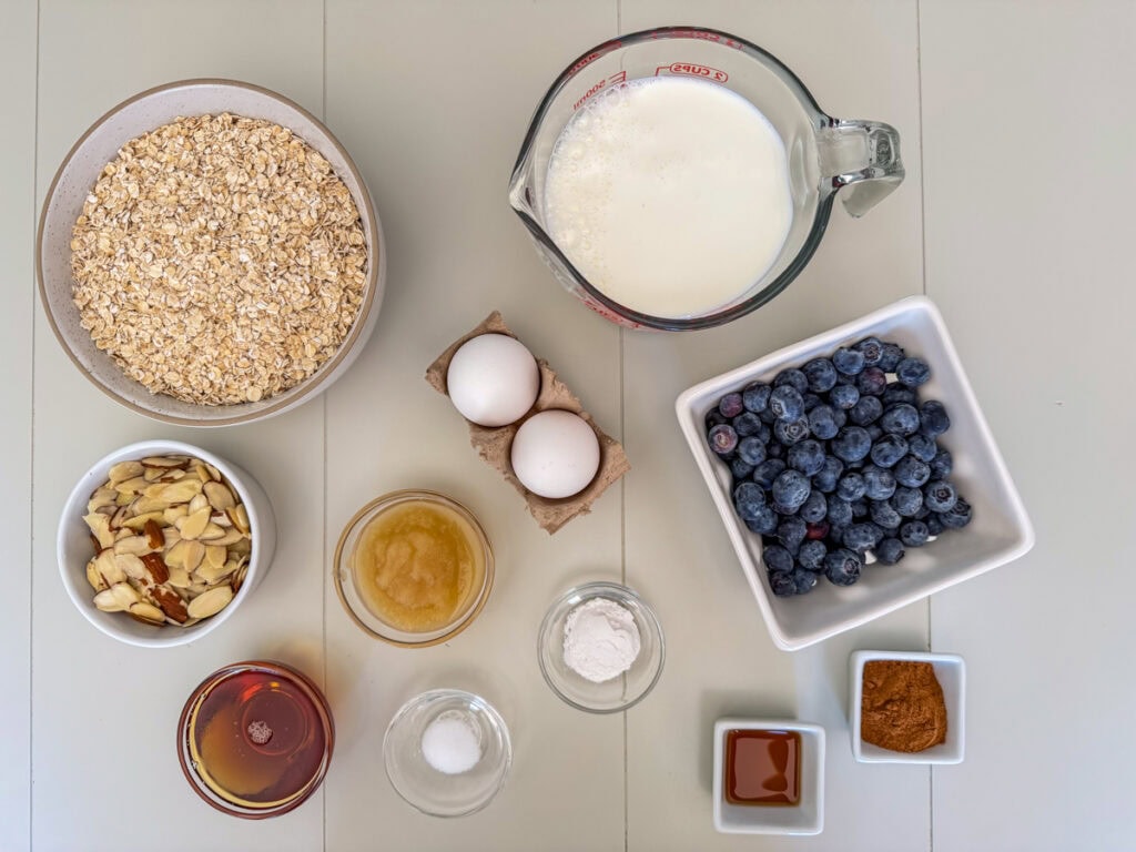 Ingredients for blueberry baked oatmeal including oats, blueberries, sliced almonds, eggs, milk, maple syrup, and cinnamon.