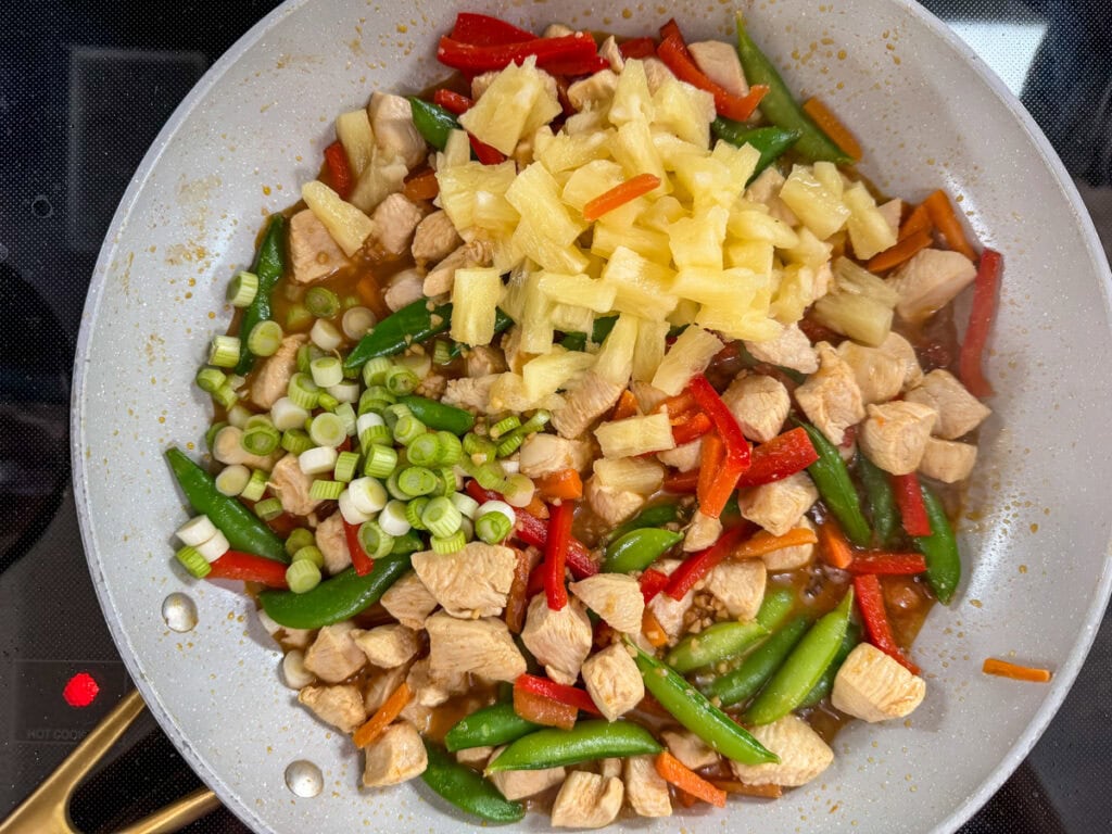 The pineapple, green onions, and sauce added to the skillet of chicken and vegetables.