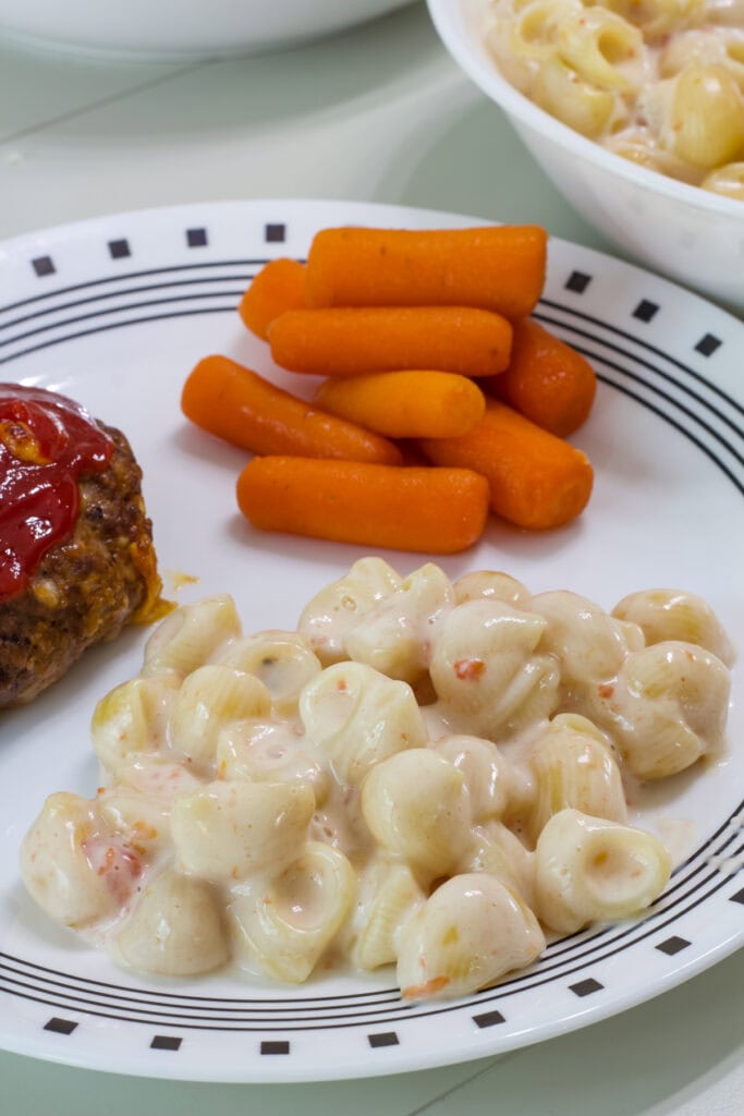 One serving of Queso Blanco Mac and Cheese on a plate with meatloaf and carrots.