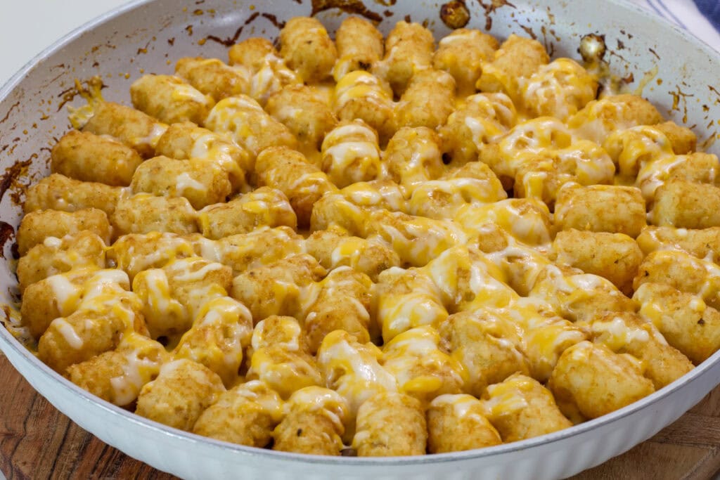 the finished tater tot casserole in a skillet on a wooden cutting board