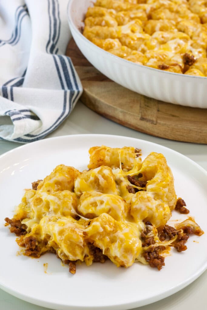 a serving of sloppy joe tater tot casserole on a white plate with the skillet in the background