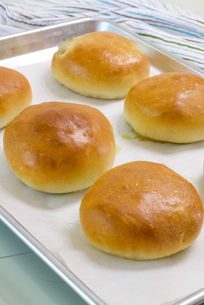 Six baked round bierocks on a parchment paper line baking sheet.