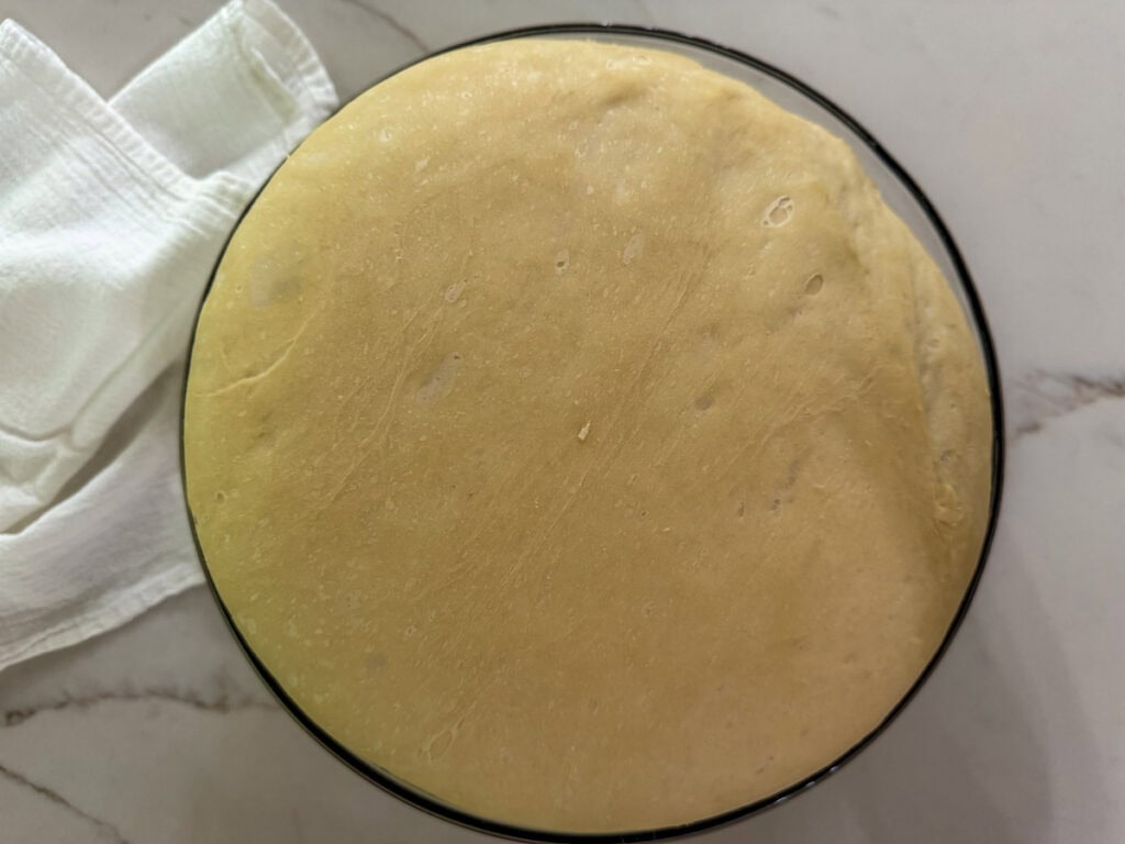 The risen dough in a large glass mixing bowl.