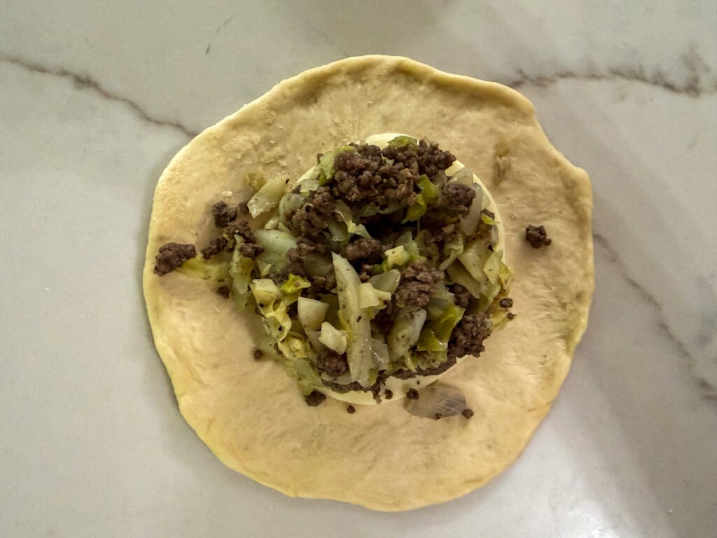 A flattened portion or dough with a slice of cheese and the filling on it.