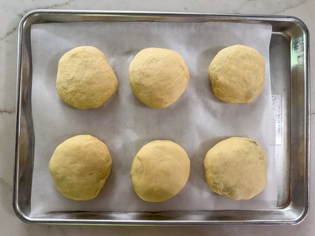 Six filled bierocks on a parchment lined rimmed baking sheet ready to go into the oven.