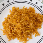 Overhead close up of a serving of Spanish rice on a white plate with black accents.