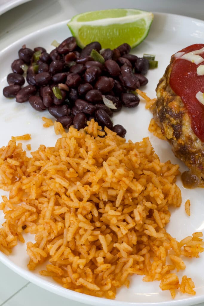A serving of Spanish rice on a plate with black beans and taco meatloaf.