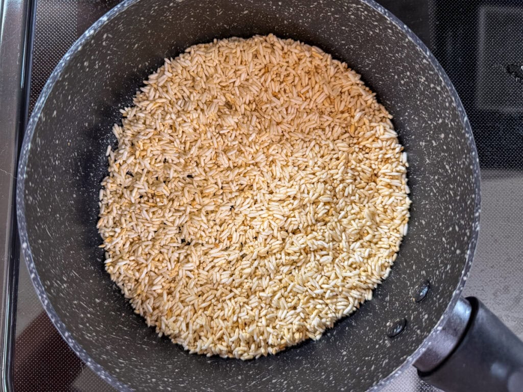 The rice and olive oil in a 2-quart saucepan after it's been toasted to show the light brown color.