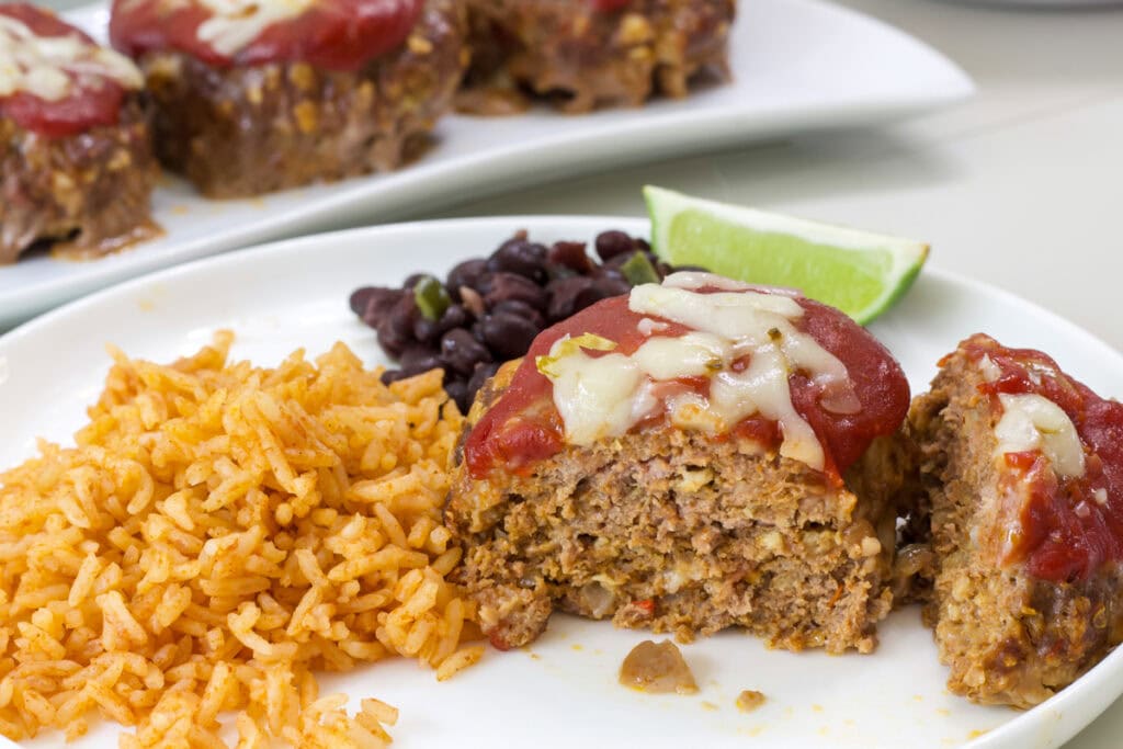 One taco meatloaf cut open so the tender inside is visible on a plate with rice, beans and a lime wedge.