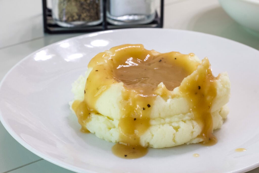 A serving of mashed potatoes with brown gravy on a white plate.