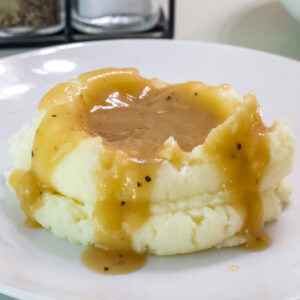 Closeup of a serving of mashed potatoes smothered in brown gravy.