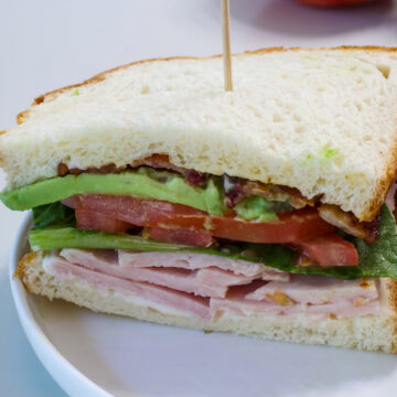 Half sandwich placed on a plate so the layers of mayo, turkey, lettuce, tomatoes, avocado and bacon are visible.