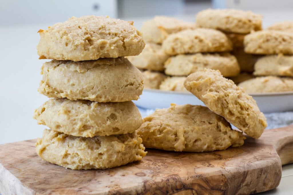 A stack of four cookies with a couple sitting next to it and a plate full of cookies in the background.