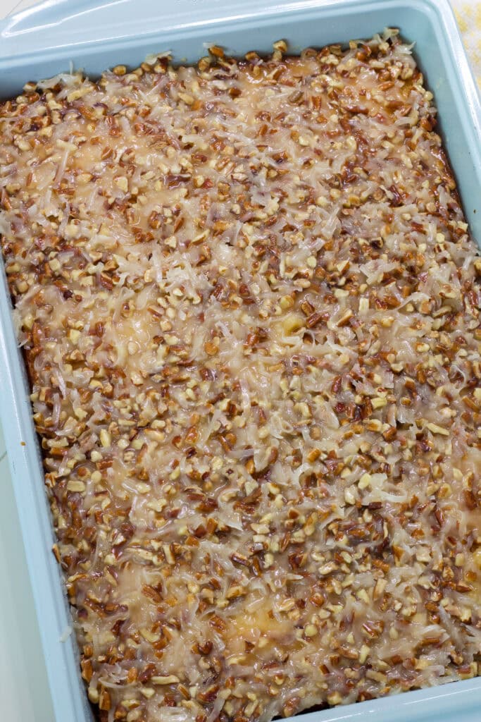 The entire uncut tornado cake with coconut pecan topping in a cake pan.