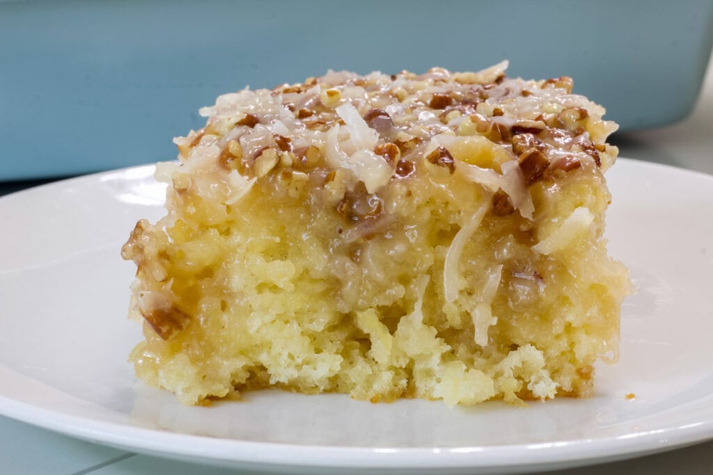 Closeup side view of one piece of tornado cake with the gooey coconut pecan topping on on a white plate.