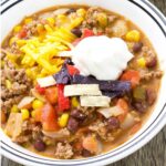 A bowl of taco chili topped with sour cream, shredded cheese, and tortilla strips.
