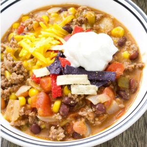 A bowl of taco chili topped with sour cream, shredded cheese, and tortilla strips.
