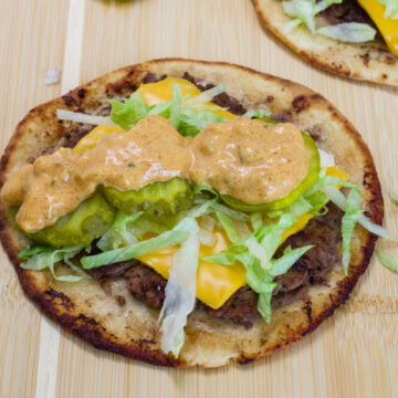 Close-up of a homemade big mac smash taco topped with pickles, shredded lettuce, cheese, and creamy big mac sauce on a wooden cutting board.