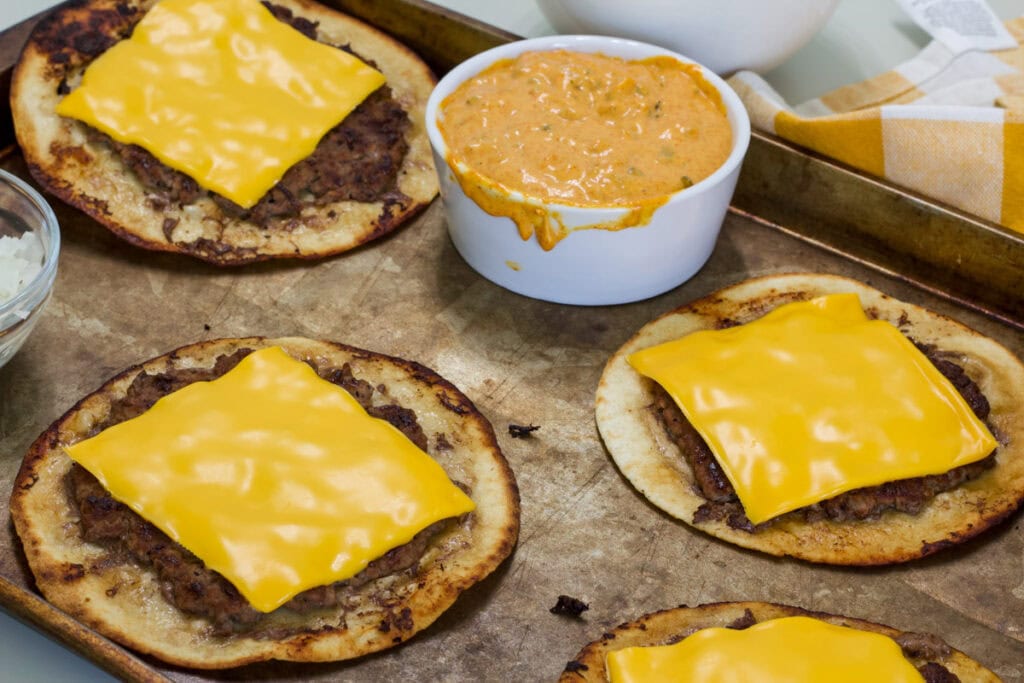 Close-up of homemade Big Mac smash tacos with melted cheese on tortillas on a baking sheet, served with Big Mac sauce.