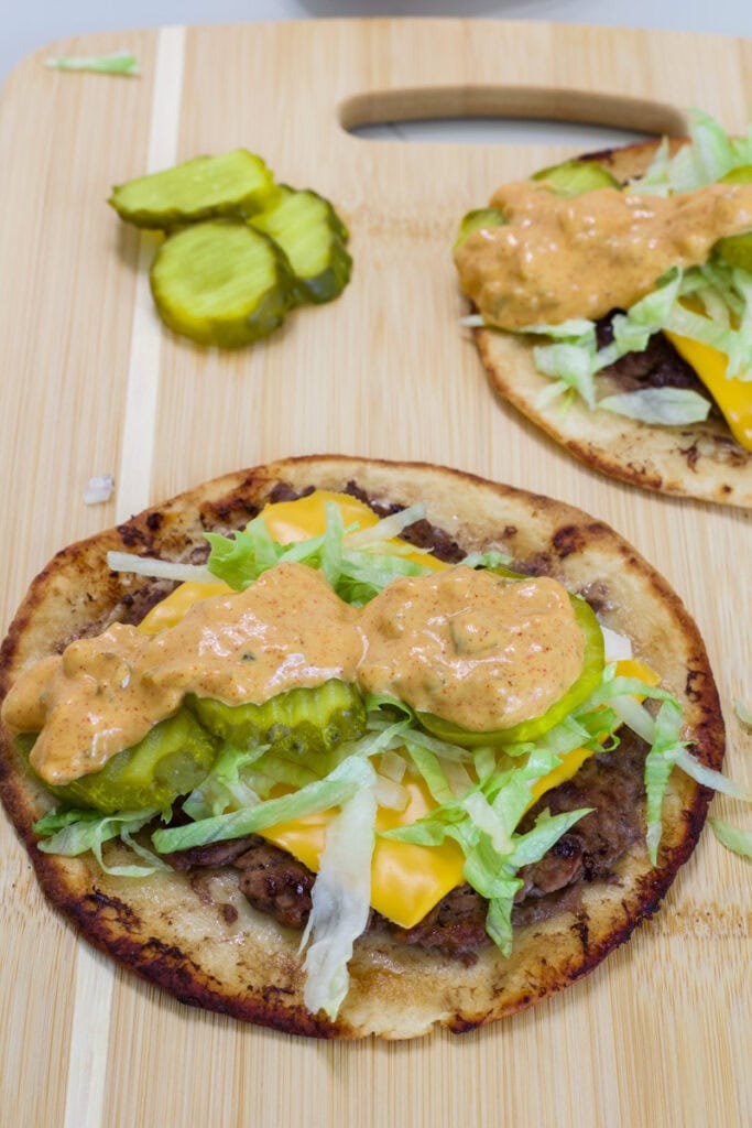 Close-up of homemade big mac smash tacos with lettuce, cheese, and Big Mac sauce on a wooden cutting board.
