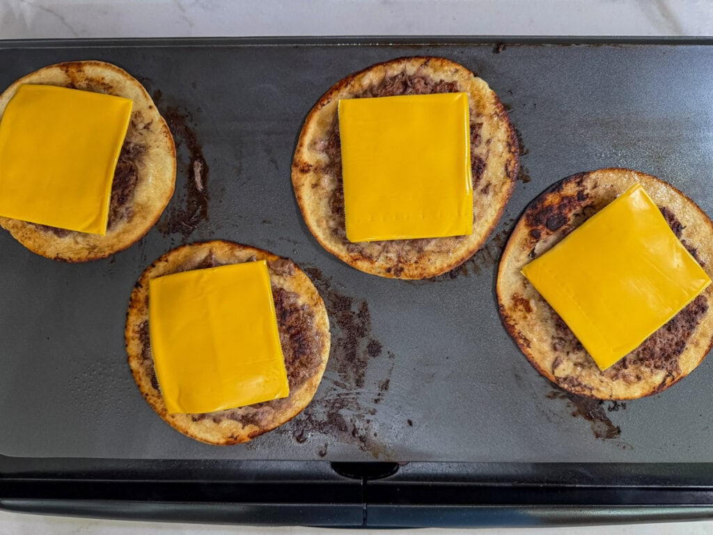 Four Big Mac smash tacos on the griddle with melted cheese on top.